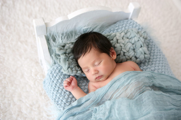 Newborn Baby Boy laying in white baby bed prop with blue blankets. Diana Henderson Photography.