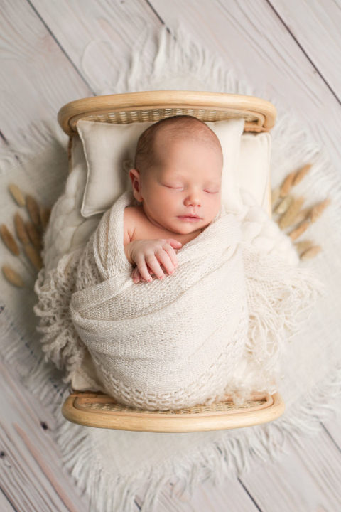 Newborn baby boy posed in a newborn prop bed during his newborn photography session.