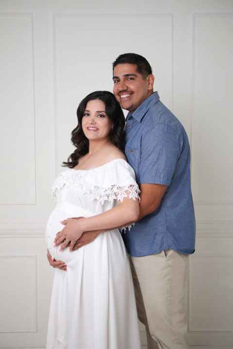 Los Angeles Studio Maternity session, white molding wall, pregnant mother in white dress, father in blue shirt.