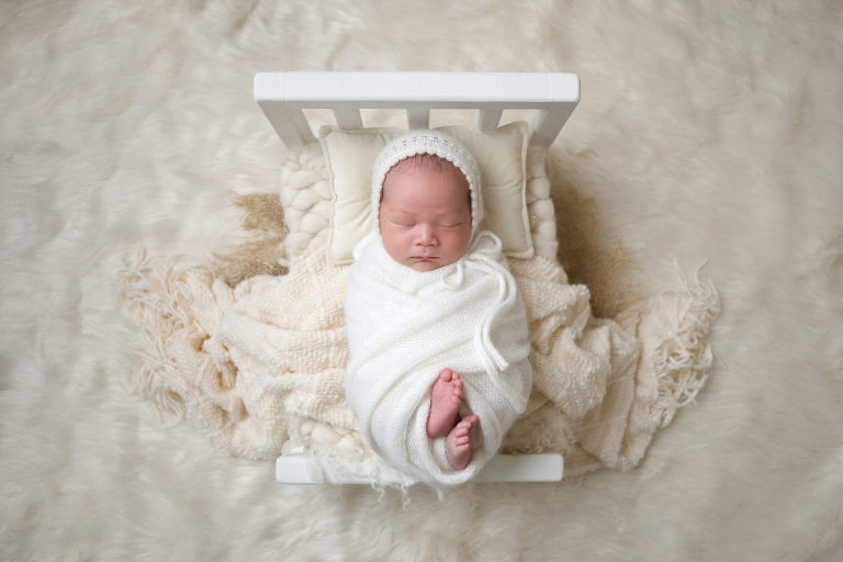 Newborn baby on white prop bed wrapped in white fabric
